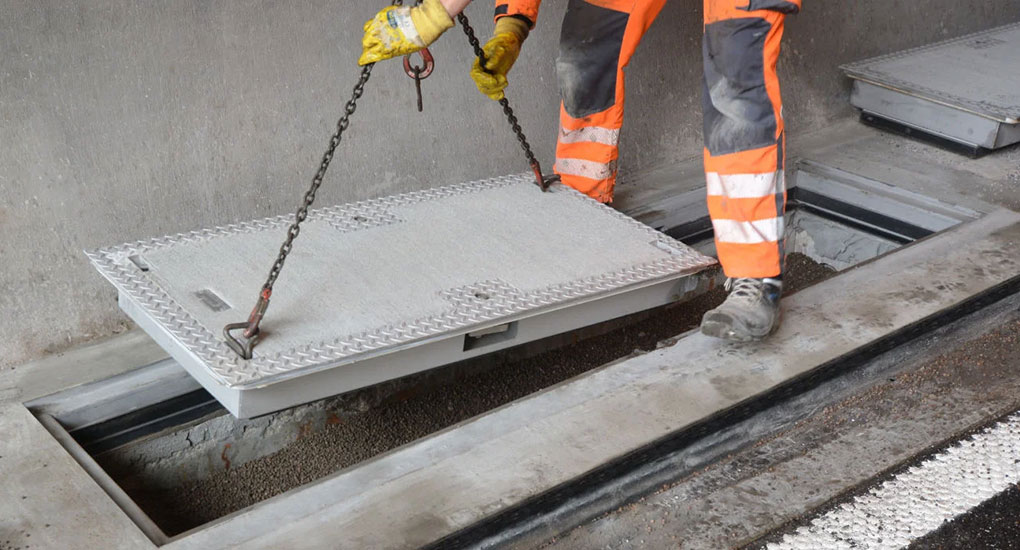 Arbeiter hebt eine schwere Tunnelabdeckung mit Ketten an.