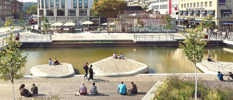 Urbaner Platz mit Wasserfläche, begehbaren Inseln, Holzdecks und Menschen, die entspannen.