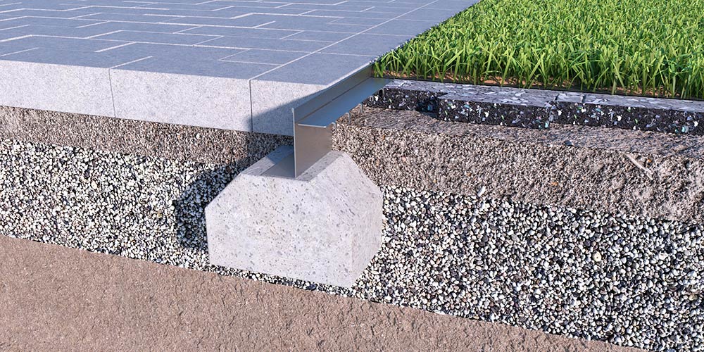 ACO Sport Shockpad-Einfassung Querschnitt einer gepflasterten Fläche mit Betonfundament und einer Raseneinfassung aus Stahl.