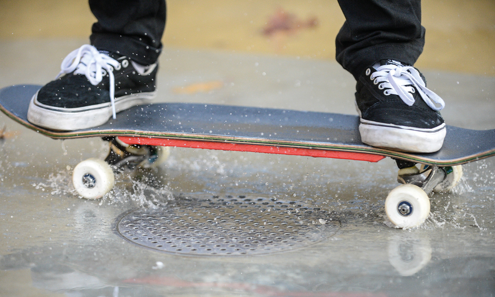 Skater fährt mit Skatebord auf nasser Oberfläche.