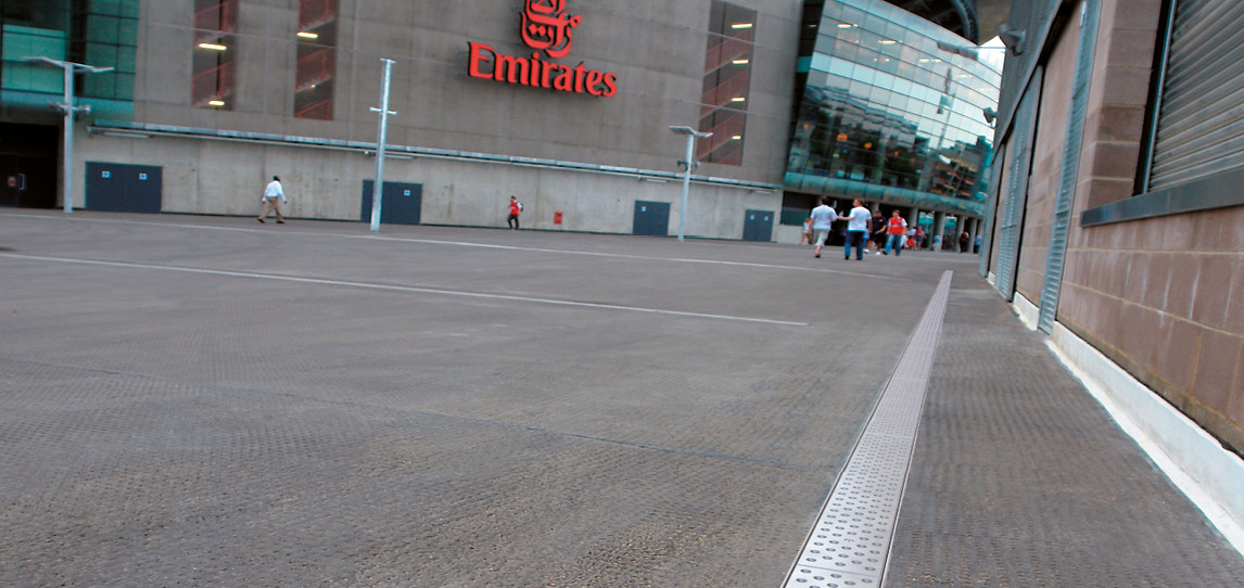 Entwässerungsrinne verlegt auf Vorplatz eines großen Gebäudes mit der Aufschrift Emirates.
