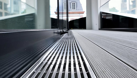 Nahaufnahme einer modernen Fassadenentwässerung mit Metallrinne an einer Glasfront.
