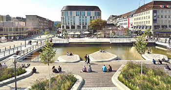 Urbaner Platz mit Wasserfläche, begehbaren Inseln, Holzdecks und Menschen, die entspannen.