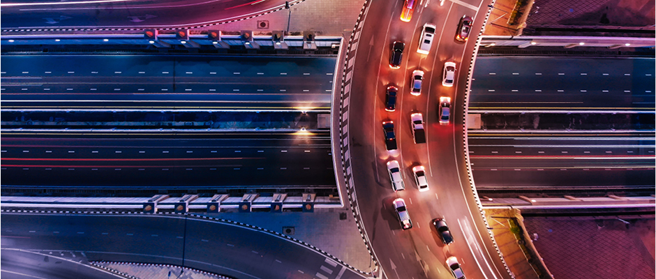 Nächtliche Luftaufnahme eines Autobahnkreuzes mit beleuchteten Fahrzeugen auf mehreren Fahrspuren.