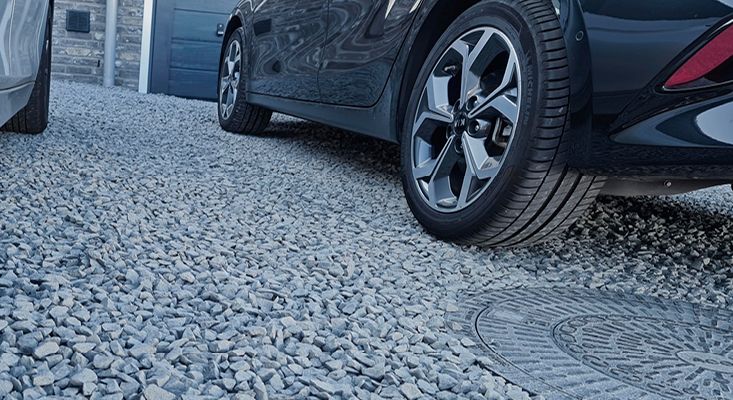 Runde Schachtabdeckung eingebettet in eine Kiesfläche, auf der zwei Autos parken.