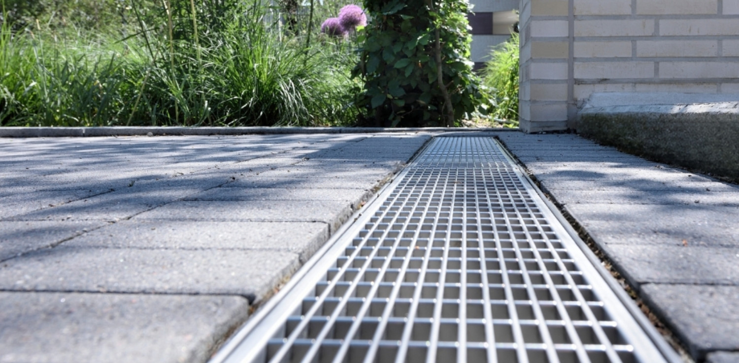 Bodennahes Foto einer Entwässerungsrinne mit Rost in gepflasterter Einfahrt, fotografiert im Fluchtpunkt.