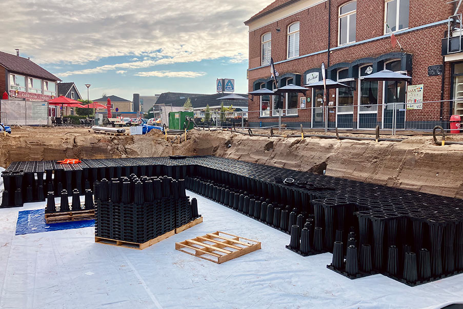 Blick in eine Baugrube mit Blockrigolensystem aus schwarzen Kunststoffhohlkörpern vor einem Backsteingebäude in einer Stadt.