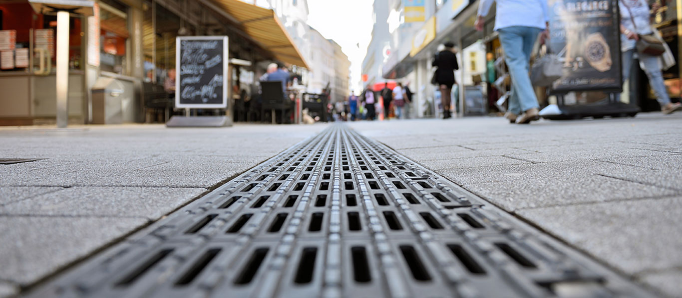 Bodennahes Foto einer Entwässerungsrinne mit Blindenleitrost in einer Fußgängerzone.