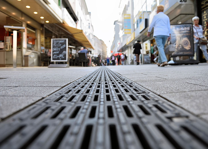 Bodennahes Foto einer Entwässerungsrinne mit Blindenleitrost in einer Fußgängerzone.