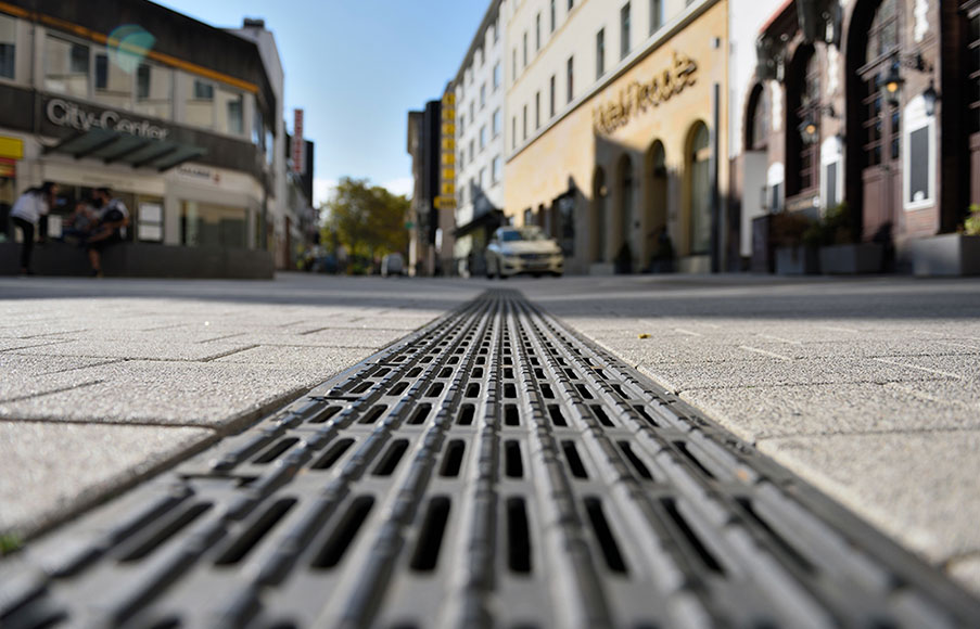 Bodennahes Foto einer Entwässerungsrinne mit Blindenleitrost in einer Fußgängerzone.