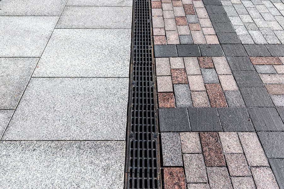 Entwässerungsrinne fügt sich harmonisch in ein Natursteinpflaster mit seinem imposanten Mosaikmuster ein.