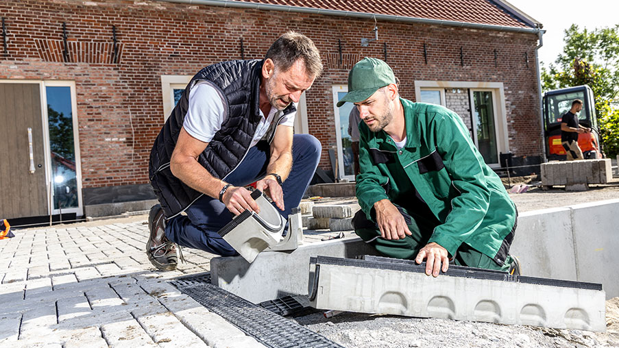 Zwei Handwerker montieren Entwässerungsrinne auf Baustelle.