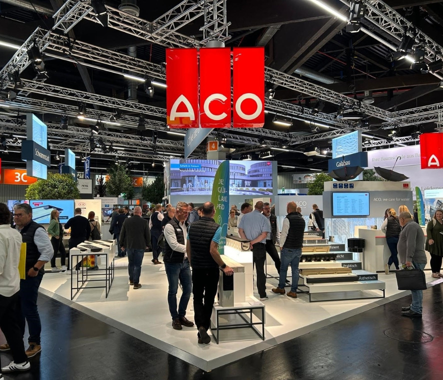 ACO Messestand auf der GaLaBau 2024. Viele Mneschen laufen über den Stand, schauen sich um und unterhalten sich. Über dem Stand hängt ein großes, rotes, leuchtendes ACO-Logo.