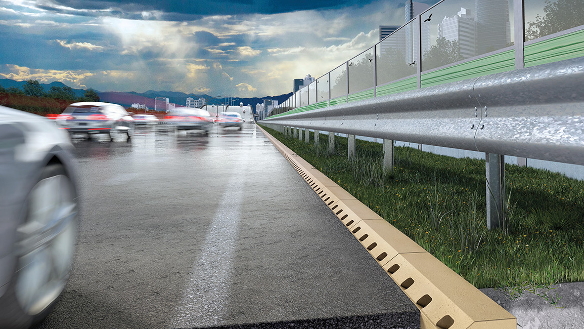 Nasse Autobahn mit vorbeifahrenden Autos, Schutzplanke und Entwässerungsrinne am Straßenrand, unter bewölktem Himmel.