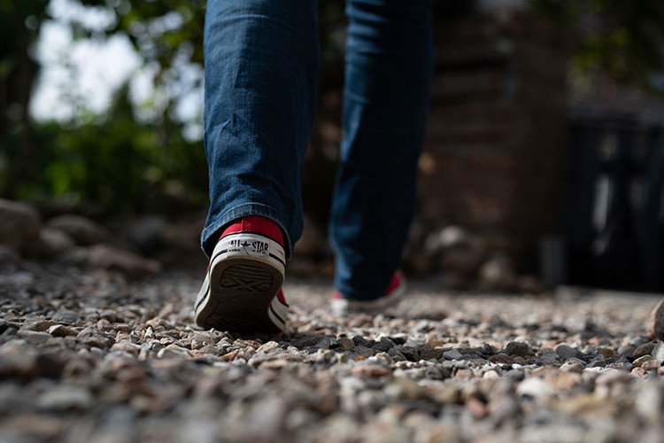 Mensch mit Jeans und Turnschuhen läuft über Kiesweg