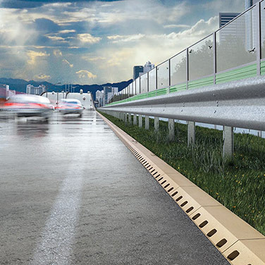 Nasse Autobahn mit vorbeifahrenden Autos, Schutzplanke und Entwässerungsrinne am Straßenrand, unter bewölktem Himmel.