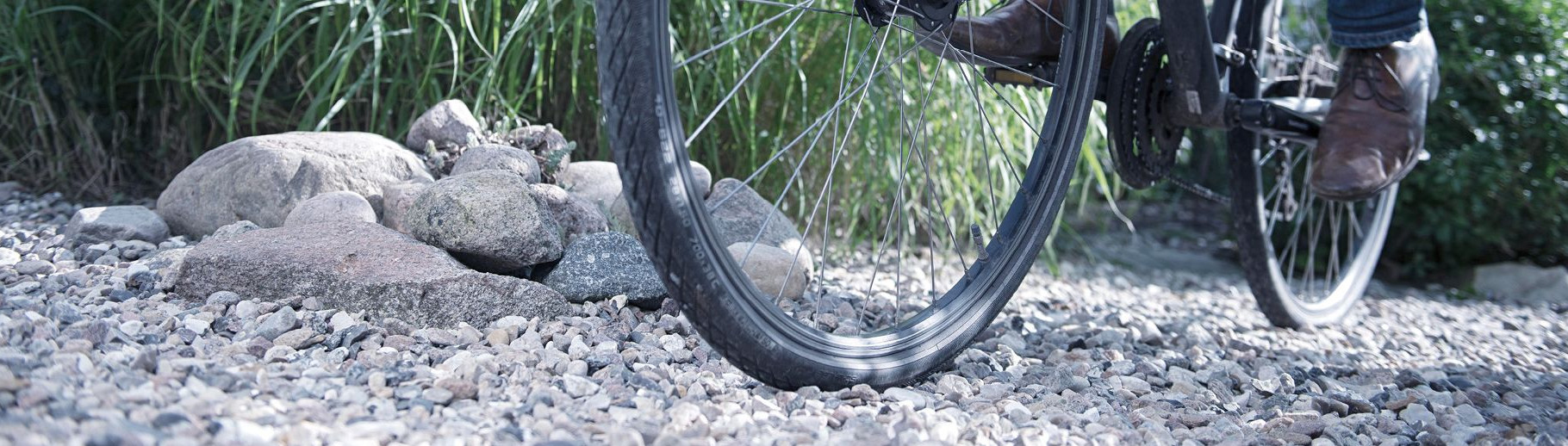 Nahaufnahme eines Fahrradreifens auf kiesigem Untergrund, Vorder- und Hinterrad mit Speichen sichtbar.