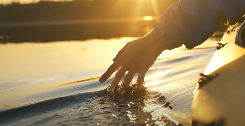 Hand gleitet durch Wasser bei Sonnenuntergang