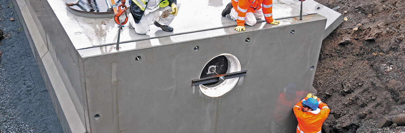 Drei Bauarbeiter in Schutzkleidung montieren ein großes Havariesystem auf einer Baustelle.