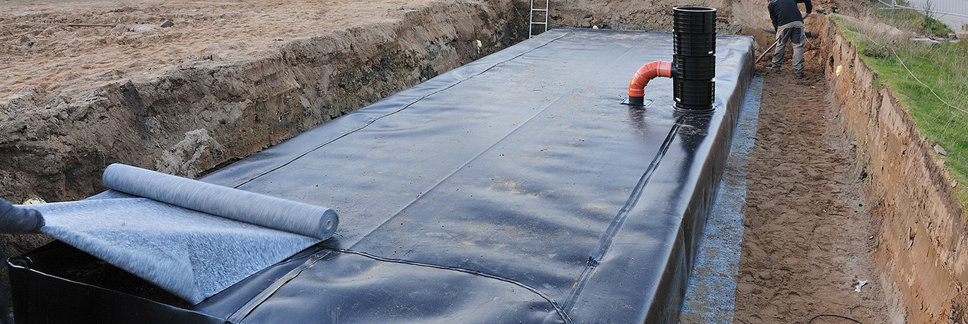 Blockrigolen mit einer Abdichtungsbahn umhüllt in einer Baugrube mit Erdreich.