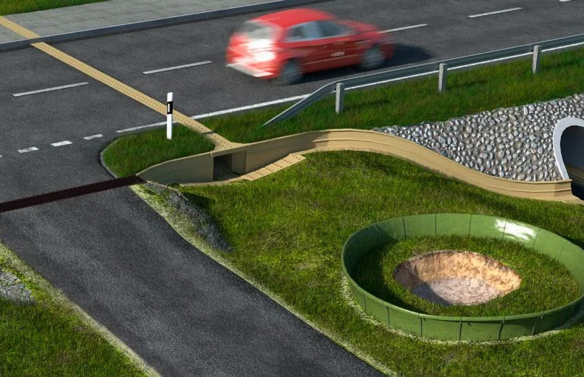 Straße mit einem fahrenden Auto führt über eine kleine Brücke, die über einen Tunnel mit steinverkleideter Einfassung führt.