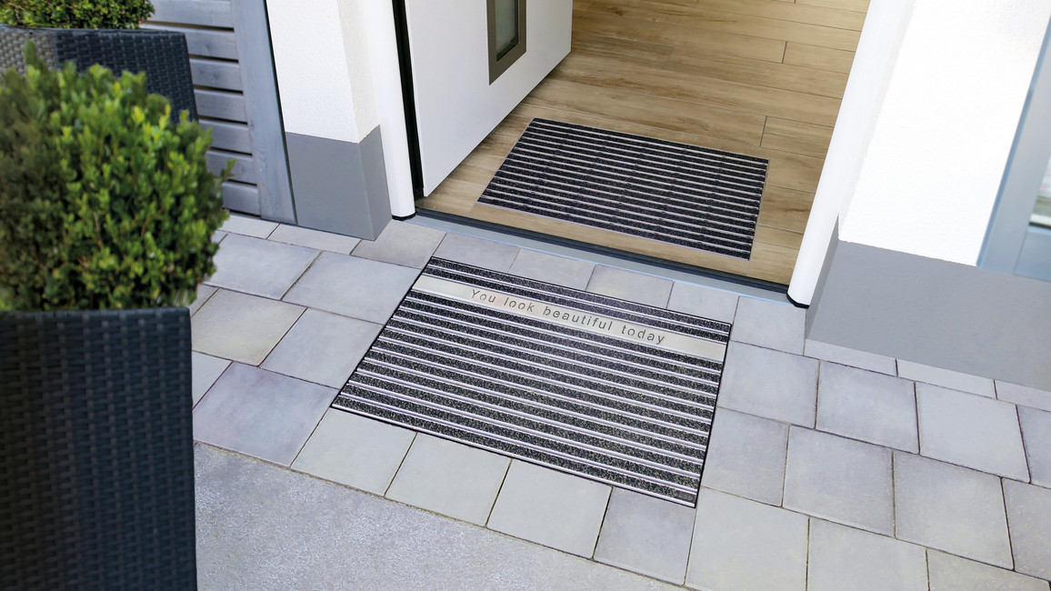 Eingangsbereich mit Innen- und Außenschuhabstreifer, der Außenschuhabstreifer mit Edelstahlleiste und eingraviertem Schriftzug.