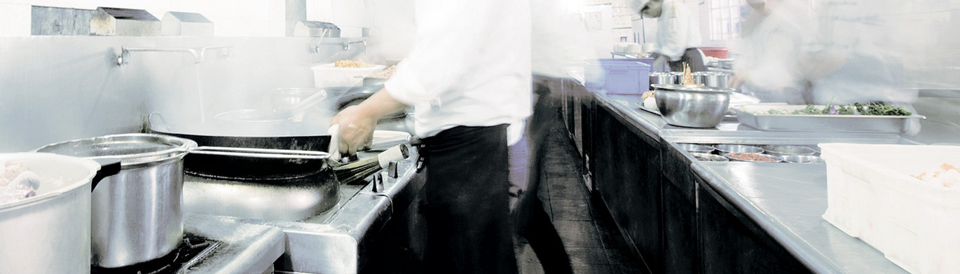 Geschäftige Restaurantküche mit Köchen, die an dampfenden Herdplatten arbeiten.