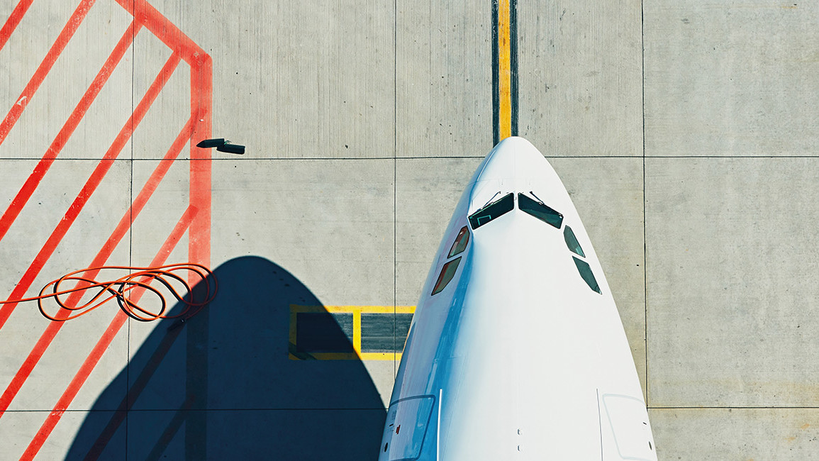 Draufsicht auf die Flugzeugnase am Boden neben roten Markierungen und Kabelschleifen auf dem Rollfeld.