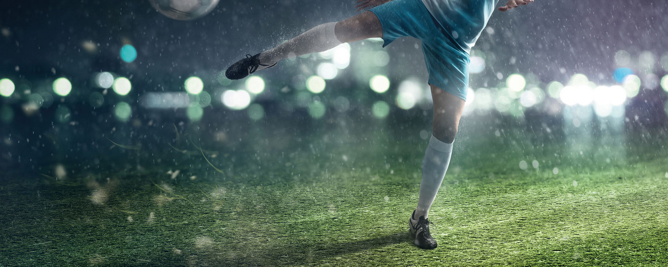 Eine Fußballspielerin schießt einen Ball. Es ist dunkel und regnerisch.