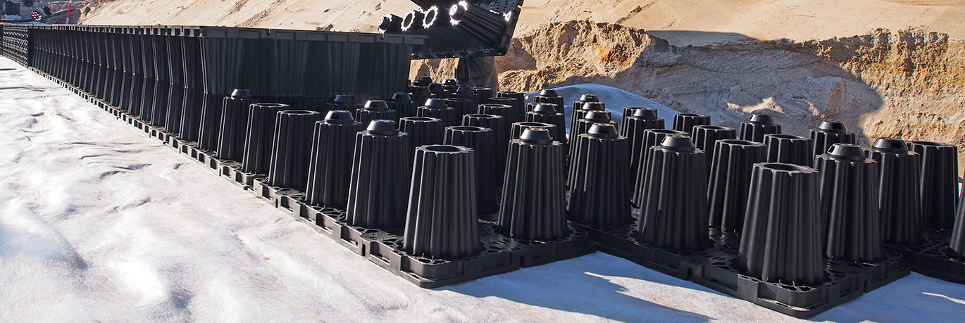 Rigolen System aus schwarzen Kunststoffhohlkörpern in einer Baugrube mit Erdreich.