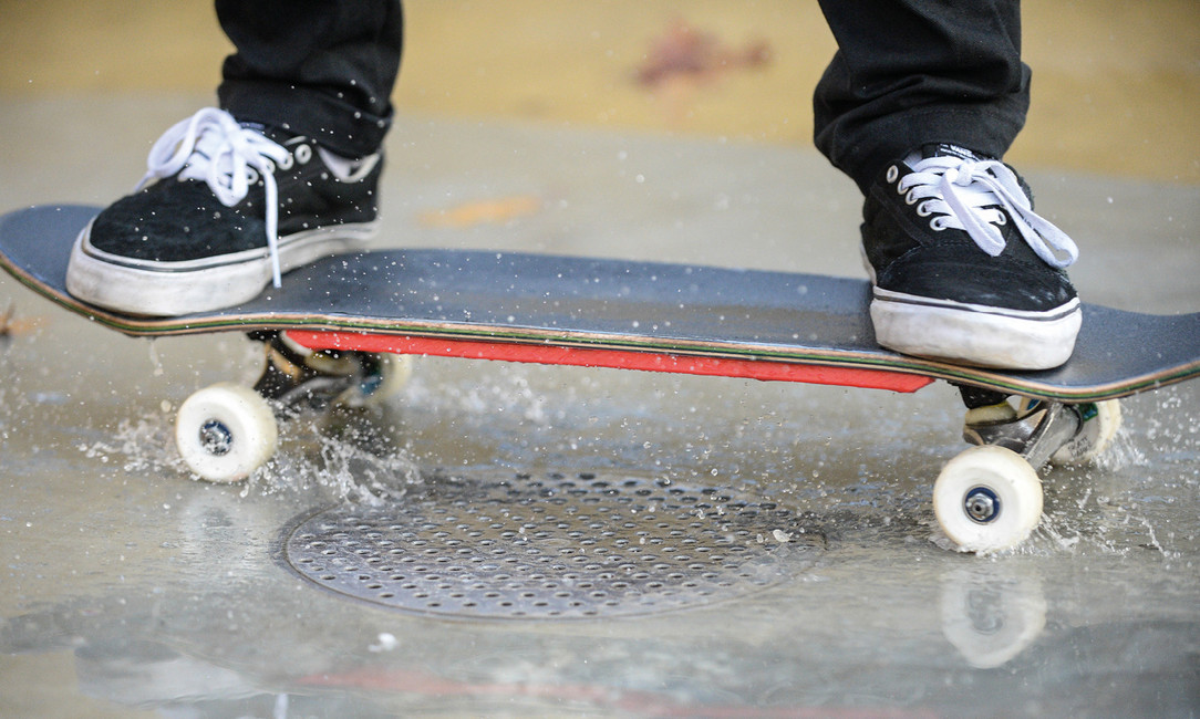 Skater fährt mit Skatebord auf nasser Oberfläche.