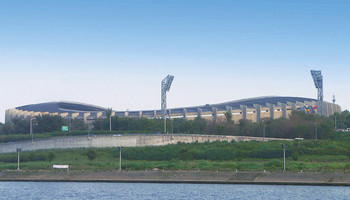 Außenansicht des Olympiastadions in Seoul, mit einer beeindruckenden, modernen Architektur. Das Stadion hat eine ovale Form und ist von markanten, geschwungenen Dachstrukturen umgeben. Die Fassade ist mit geometrischen Mustern gestaltet.