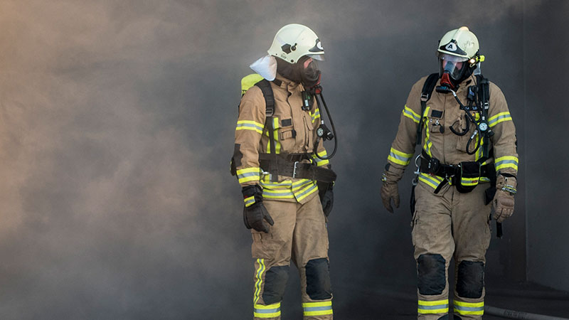 zwei feuerwehrmaenner umgeben von Rauch